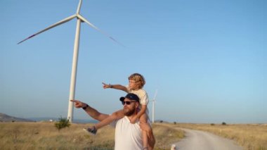 Omzunda Çocuğunu Taşıyan ve Rüzgar Tarlasında Yürüyen Adam. Mutlu Baba ve Kız Daha Çevresel, Sürdürülebilir Enerjide Birlikte Temiz Hava ve Zamanın Tadını Çıkarıyorlar