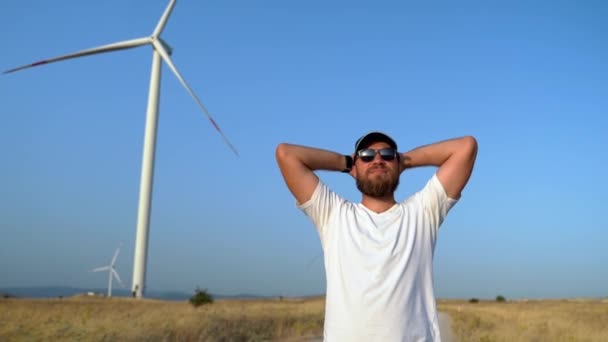 ハッピーリラックスした髭の男は フィールドウインドミルで自然の日没を楽しみながら腕を上げます 環境に優しいエネルギー 持続可能な消費 — ストック動画