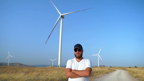 風車の風力発電機が付いている分野の田舎の道の上の箱の上に十字の腕に立っている幸せな自信のある男 環境に優しいエネルギーパワー 持続可能な消費 — ストック動画