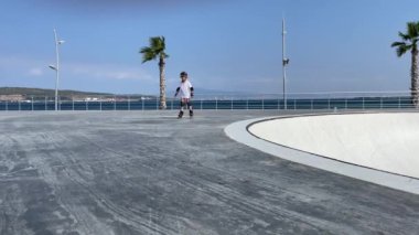 Küçük kız yaz güneşli bir günde halka açık kaykay parkında paten kaymayı öğreniyor. Çocuklar için spor aktivitesi. Hobi ve sağlıklı yaşam tarzı