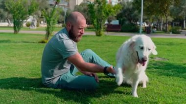 Evcil hayvan sahibi adam, yaz boyunca bahçe parkında köpeğiyle Golden Retriever oynuyor..