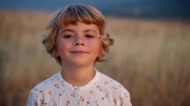 Rahat çocuk kız temiz hava soluyor kameraya bakıyor mutlu mavi gökyüzü gün batımına gülümsüyor yazın kırsal alan üzerinde alacakaranlık. Rüya, özgürlük ve seyahat konsepti, tarım ve organik