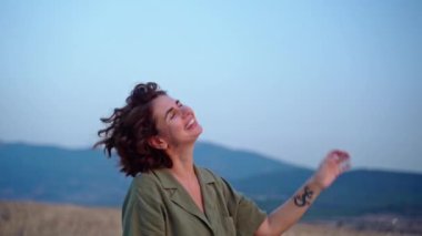 Rahat bir kadın, yaz mevsiminde dağlarda gün batımında kollarını kaldırarak temiz hava soluyor. Hayal kurmak, özgürlük ve seyahat kavramı. Kadın ruhsal sağlığı.