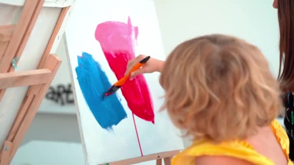 アートスクールの先生が絵画でアートクラスの子供たちを助けます 女性は子供にアクリルペンキを作成し 働くように教えます 小学生のグループは 彼らの助けを描き 着色する方法を学びます — ストック動画