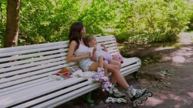 Anne ve kızı halka açık parkta paten kaydıktan sonra bankta atıştırıyorlar. Aile eğlencesi spor aktivitesi hafta sonu. Negatif alanı kopyala