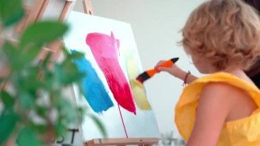 Sanat okulundaki öğretmen resim derslerinde çocuklara yardım ediyor. Kadın çocuğa akrilik boyayla yaratmayı ve çalışmayı öğretiyor. Bir grup ilkokul çocuğu resim çizmeyi ve boyama yardımını öğreniyorlar.
