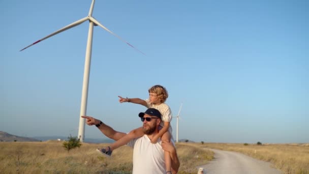 子供の少女を肩に乗せて風の農場を歩いている男 幸せな父と娘 より環境にやさしい持続可能な効率的なエネルギーで一緒にクリーンな空気を楽しむ — ストック動画