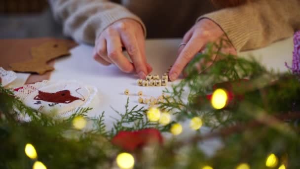 クリスマスのガーランドライトと松の木の枝の上の手紙と木製のブロックで幸せな新年を作るクローズアップ女性の手 デコレータは オンラインショッピングのための装飾を作成します — ストック動画