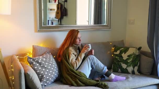 在温暖的家 穿着暖和的毛衣 坐在靠窗的沙发上 裹着毛毯 看着外面 穿着暖和的毛衣 在十二月的冬天热身 文娱休憩 — 图库视频影像