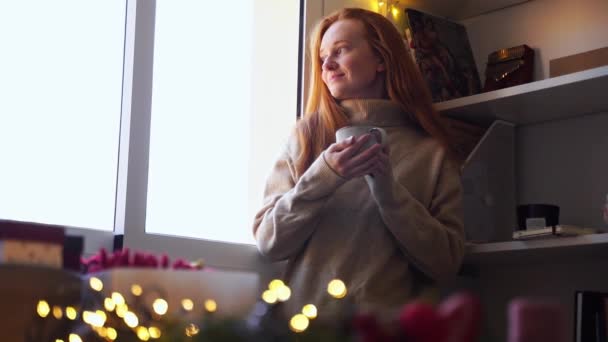 Przytulna Młoda Rudowłosa Kobieta Pijąca Gorącą Herbatę Przy Oknie Wyglądająca — Wideo stockowe