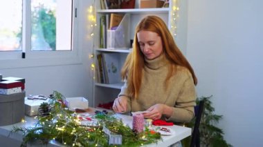 Kızıl kadın el yapımı Noel oyuncağı yapıyor. Mutlu yıllar çevre dostu malzemelerle süsleniyor. Dekoratör mağazada online alışveriş için hediyeler yaratıyor. Needlewoman ailesi için el yapımı.