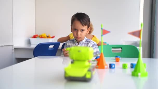 技術教育クラスの電子リモート玩具車のコントロールパネルで遊ぶ優れたモータースキルを開発する子供の少年 幼稚園児がテクノロジーを探求する最初のステップ — ストック動画