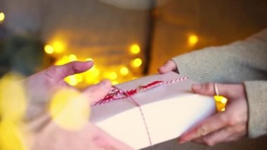 Yakın plan kadın elleri, erkeklere Noel hediyesi olarak hafif çelenk veriyor. Samimi, samimi ve sevgi dolu bir çift. Birbirinizi sürpriz hediyelerle tebrik edin..