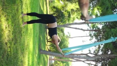 Deneyimli kadın eğitmen, hamaklardaki kadınlar için parktaki hava yogası seansına liderlik ederek güvenli bir yaklaşım sağlıyor. Esneme dersleri güvenliği artırır. Sağlık bakımı