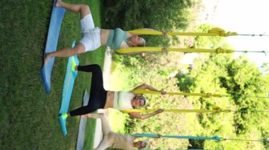 Kadınlar parkın dışında birlikte antrenman yapıyor. Yoga ve hamaklarda gerinme. Kadın sağlığı için spor. Egzersiz stresin azaltılmasına yardımcı olur, içindeki uyumu korur ve genel refaha katkıda bulunur.