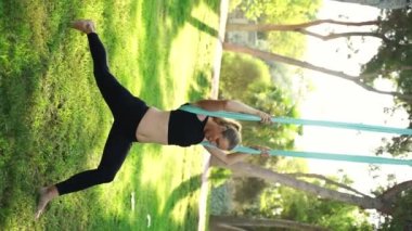Deneyimli kadın eğitmen, hamaklardaki kadınlar için parktaki hava yogası seansına liderlik ederek güvenli bir yaklaşım sağlıyor. Esneme dersleri güvenliği artırır. Sağlık bakımı