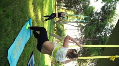 Deneyimli kadın eğitmen, hamaklardaki kadınlar için parktaki hava yogası seansına liderlik ederek güvenli bir yaklaşım sağlıyor. Esneme dersleri güvenliği artırır. Sağlık bakımı