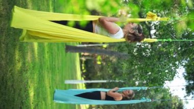 Kadınlar parkın dışında birlikte antrenman yapıyor. Yoga ve hamaklarda gerinme. Kadın sağlığı için spor. Egzersiz stresin azaltılmasına yardımcı olur, içindeki uyumu korur ve genel refaha katkıda bulunur.