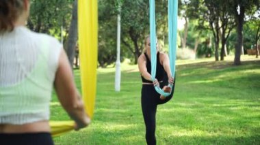 Deneyimli kadın aero yoga esneme antrenörü Asana 'nın hamakta olduğunu gösteriyor. Kamu parkında kadın grup çalışması. Yetişkinler için iş çıkışı aktiviteleri. Spor egzersizleri sağlık vücut bakımını sürdürür