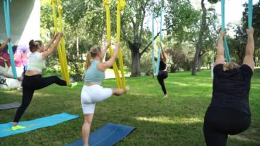 Deneyimli kadın yoga germe eğitmeni, hamaklardaki kadınlar için parktaki hava yogası antrenmanına öncülük ederek güvenli bir yaklaşım sağlıyor. Spor egzersizleri güvenlik yaratır. Sağlık bakımı