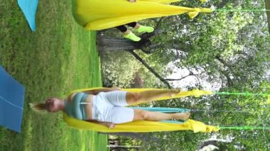 Deneyimli kadın yoga germe eğitmeni, hamaklardaki kadınlar için parktaki hava yogası antrenmanına öncülük ederek güvenli bir yaklaşım sağlıyor. Spor egzersizleri güvenlik yaratır. Sağlık bakımı