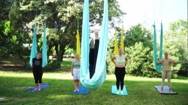 Deneyimli kadın aero yoga esneme antrenörü Asana 'nın hamakta olduğunu gösteriyor. Kamu parkında kadın grup çalışması. Yetişkinler için iş çıkışı aktiviteleri. Spor egzersizleri sağlık vücut bakımını sürdürür