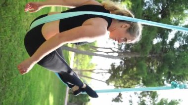 Deneyimli kadın yoga germe eğitmeni, hamaklardaki kadınlar için parktaki hava yogası antrenmanına öncülük ederek güvenli bir yaklaşım sağlıyor. Spor egzersizleri güvenlik yaratır. Sağlık bakımı Dikey