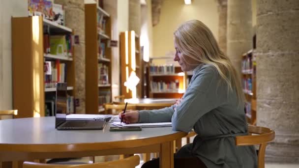 在图书馆工作 查找信息的成熟女教师 成人教育 上了年纪的学生在准备大学的考试 自由职业者获得知识 — 图库视频影像