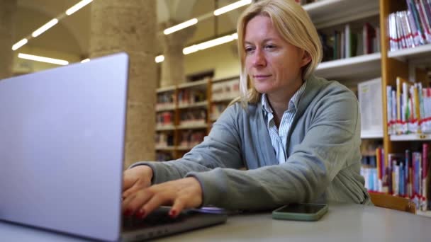 在图书馆学习新教育科目的成年女生中年妇女在网上使用笔记本电脑学习和研究科学资料 提高专业资格 — 图库视频影像