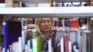 Kütüphanede ya da kitapçıda kitap seçen orta yaşlı bir kadın. Yetişkinler kitaba göz atıyor. Kitapçıda okuyan öğrenci. Edebiyat gibi olgun bir kadın, kütüphanede kitap seçiyor.