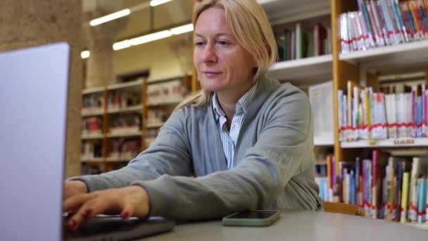 女性の成人学生は インターネット上の科学資料の研究と研究にノートパソコンを使用して図書館の中年女性の新しい教育主題を学びます プロ資格をアップグレードする — ストック動画