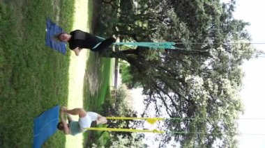 Kadınlar parkın dışında birlikte antrenman yapıyor. Yoga ve hamaklarda gerinme. Kadın sağlığı için spor. Egzersiz stresin azaltılmasına yardımcı olur, içindeki uyumu korur ve genel refaha katkıda bulunur.