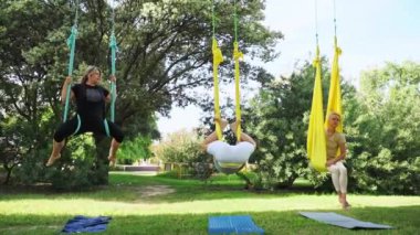 Deneyimli kadın yoga germe eğitmeni, hamaklardaki kadınlar için parktaki hava yogası antrenmanına öncülük ederek güvenli bir yaklaşım sağlıyor. Spor egzersizleri güvenlik yaratır. Sağlık bakımı