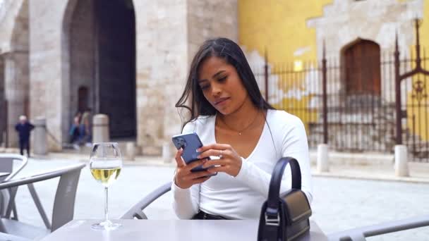 カフェパティオに座っている携帯電話を使用して美しいラテンアメリカの女性 ソーシャルメディアをスクロール モバイルアプリを使用して オンラインメニューで注文 友達とチャット コンテンツを作成 リール Eで旅行 — ストック動画