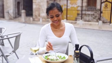 İspanyol genç kadın yemek aşığı açık hava restoranında yemeğin tadını çıkarıyor. Vejetaryen yemeği yeşil salata yer. Günlük mutlu sağlıklı alışkanlıklar. Kafeterya terasında güzel bir Latin Amerikalı kadın.
