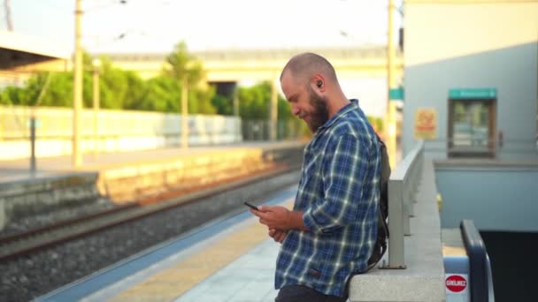 城里人背着背包在月台上等地铁列车 一个在公共交通工具上使用手机上班的成年人 早上的城市生活就像市民依赖地铁一样 — 图库视频影像