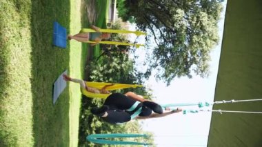 Kadınlar parkın dışında birlikte antrenman yapıyor. Yoga ve hamaklarda gerinme. Kadın sağlığı için spor. Egzersiz stresin azaltılmasına yardımcı olur, uyumu korur ve dikey refahı sağlar