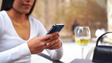 Kafe avlusunda telefon kullanan güzel Latin Amerikalı kadın. Sosyal medya kaydırma, mobil uygulama kullanma, çevrimiçi menü siparişi verme, arkadaşlarla sohbet etme, içerik oluşturma, makara oluşturma, e