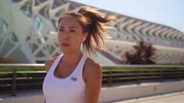 Asyalı yetişkin kadın koşucu spor kıyafetleriyle koşuyor güneşli bir sabah uykusunda yüksek teknoloji şehir arka planında. Koşu maratonu, dayanıklılık, kalp egzersizi sağlıklı yaşam tarzı.