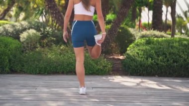 Asyalı yetişkin kadın sporcu kıyafetleriyle koşuyor. Güneşli sabah antrenmanlarından önce kaslarını ve eklemlerini ısıtıyor. Palmiye kentinin yüksek teknolojili koşu bandı. Yetişkinler için kentsel sağlıklı yaşam tarzı