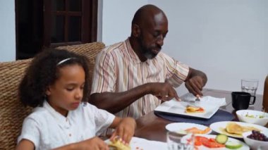Afro-Amerikan beyaz aileler ve çocuklar hafta sonu birlikte öğle yemeği kahvaltısı yiyor. Aile geleneği, çocuklar için sağlıklı yiyecekler, boş zaman aktivitesi, bakım ve ilişkiler