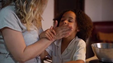 Kafkasyalı anne Afrikalı Amerikalı kızıyla oynarken çok ırklı aile çocukları da evdeki rahat mutfakta krep kahvaltısı hazırlıyor. Çok ırklı aile geleneği hafta sonu tatili