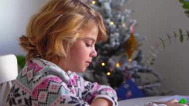 Noel Baba 'ya yeni yıl tatili için mektup yazan çocuk, rahat Noel süslemeleri ve ışıkları, renkli kalemler çizen kız, Noel Baba' ya hediyeler hazırlayan çocuk,