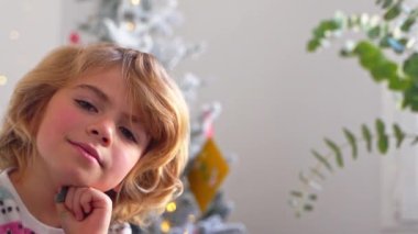 Gülümseyen ilkokul çocuğunun portresi Noel ağacı süsleme arkaplanından kameraya bakıyor, reklam için negatif alanı kopyalıyor Noel Baba 'ya yeni yıl tatili için mektup yazıyor, rahat bir ev.