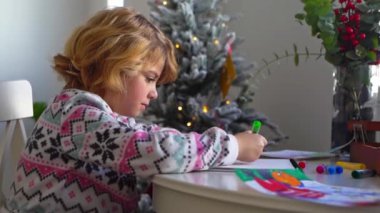 Noel Baba 'ya yeni yıl tatili için mektup yazan çocuk, rahat Noel süslemeleri ve ışıkları, renkli kalemler çizen kız, Noel Baba' ya hediyeler hazırlayan çocuk,