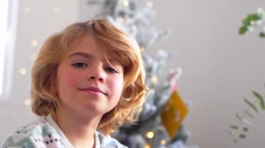Gülümseyen ilkokul çocuğunun portresi Noel ağacı süsleme arkaplanından kameraya bakıyor, reklam için negatif alanı kopyalıyor Noel Baba 'ya yeni yıl tatili için mektup yazıyor, rahat bir ev.