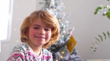 Gülümseyen ilkokul çocuğunun portresi Noel ağacı süsleme arkaplanından kameraya bakıyor, reklam için negatif alanı kopyalıyor Noel Baba 'ya yeni yıl tatili için mektup yazıyor, rahat bir ev.