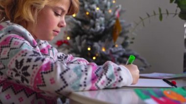Noel Baba 'ya yeni yıl tatili için mektup yazan çocuk, rahat Noel süslemeleri ve ışıkları, renkli kalemler çizen kız, Noel Baba' ya hediyeler hazırlayan çocuk,