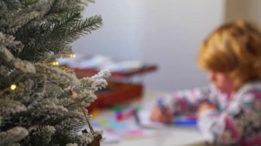 Noel Baba 'ya yeni yıl tatili için mektup yazan çocuk, rahat Noel süslemeleri ve ışıkları, renkli kalemler çizen kız, Noel Baba' ya hediyeler hazırlayan çocuk,