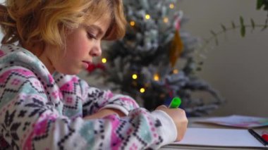 Noel Baba 'ya yeni yıl tatili için mektup yazan çocuk, rahat Noel süslemeleri ve ışıkları, renkli kalemler çizen kız, Noel Baba' ya hediyeler hazırlayan çocuk,